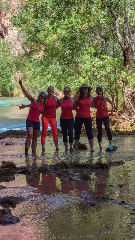 Group of five women in red shirts wading in clear water